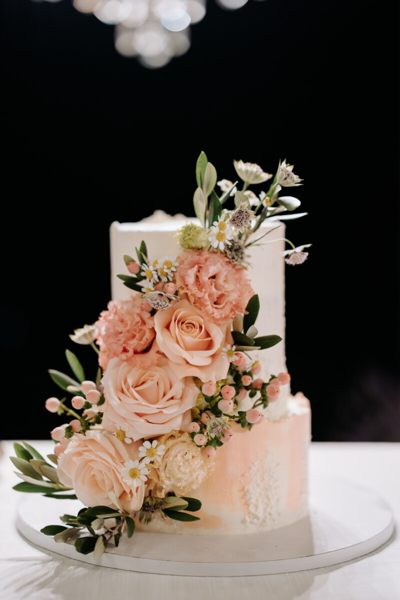 Two-tiered cake adorned with pink and white flowers on a white cake stand.