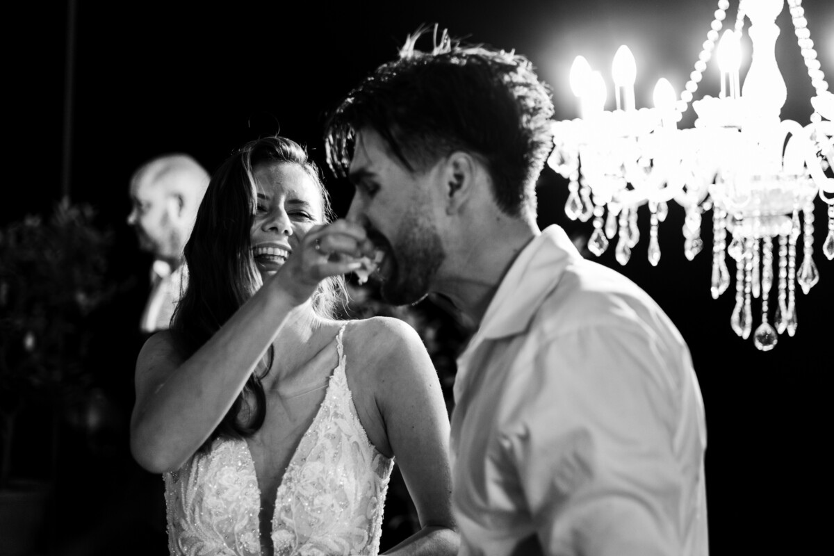 A couple laughing and enjoying a moment while dancing under a chandelier during a celebration.