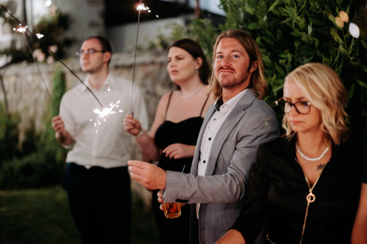 A group of individuals holding sparklers during an evening event in a garden setting.